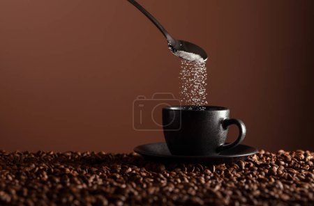 Photo for Sugar is poured into a cup of coffee. Black cup of coffee on the table with scattered beans. Copy space. - Royalty Free Image