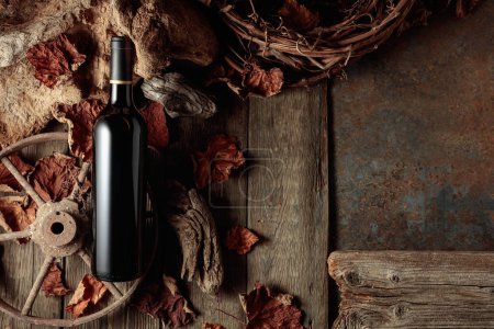 Foto de Botella de vino tinto sobre un fondo rústico vintage con madera vieja y hojas de vid secas. Concepto de vino viejo. Copiar espacio. - Imagen libre de derechos