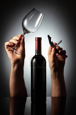Téléchargez les photos : Bouteille non ouverte de vin rouge et les mains avec tire-bouchon et verre à vin. Concept du thème du vin. - en image libre de droit