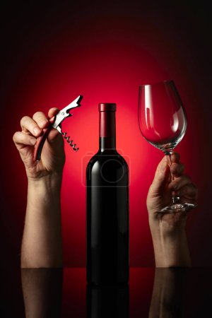 Photo for Unopened bottle of red wine and hands with corkscrew and wine glass. Concept of the wine theme. - Royalty Free Image