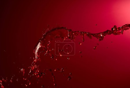 Foto de Salpicadura de vino tinto sobre un fondo rojo oscuro. Copiar espacio. - Imagen libre de derechos