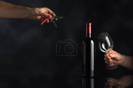 Téléchargez les photos : Bouteille non ouverte de vin rouge et les mains avec tire-bouchon et verre à vin. Concept du thème du vin. Espace de copie. - en image libre de droit
