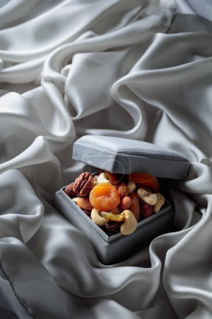 Foto de Frutas y frutos secos en una caja de regalo sobre un paño gris. - Imagen libre de derechos
