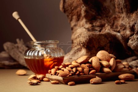 Photo for Almond nuts in a wooden dish and honey in a glass jar. Still life with fresh-cropped nuts and old snags. - Royalty Free Image