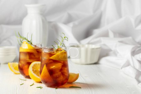 Photo for Iced tea or alcoholic cocktail with ice, rosemary and lemon slices on the white table. Fresh healthy cold lemon beverage. Tea with ice and lemon. - Royalty Free Image