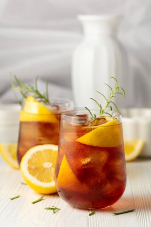 Photo for Iced tea or alcoholic cocktail with ice, rosemary and lemon slices on the white table. Fresh healthy cold lemon beverage. Tea with ice and lemon. - Royalty Free Image