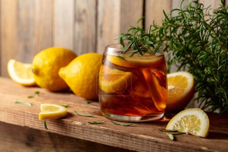 Photo for Iced tea or alcoholic cocktail with ice, rosemary and lemon slices on a old wooden table. Fresh healthy cold lemon beverage. Tea with ice and lemon. - Royalty Free Image