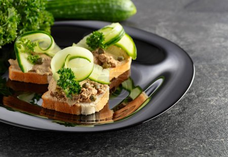 Photo for Open sandwiches with pate, fresh cucumber, capers, and parsley. Toasts with pate on a black plate. - Royalty Free Image