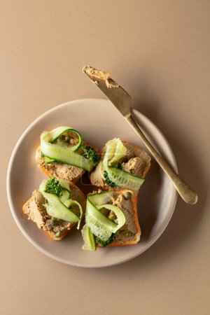 Photo for Open sandwiches with pate, fresh cucumber, capers, and parsley. Toasts with pate on a beige background. Top view, copy space. - Royalty Free Image