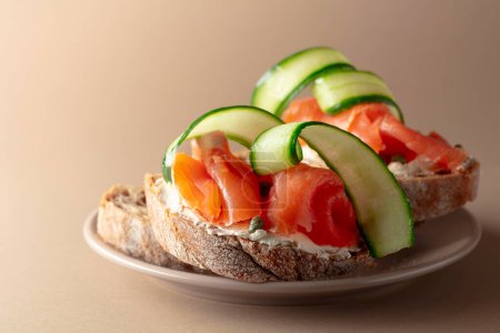 Photo for Sandwiches with smoked trout, cream cheese, fresh cucumber and capers on a beige plate. - Royalty Free Image
