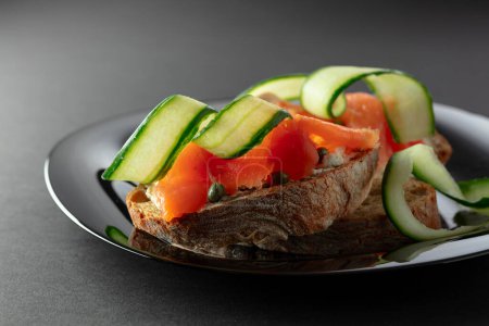Photo for Sandwiches with smoked trout, cream cheese, fresh cucumber, and capers on a black plate. - Royalty Free Image