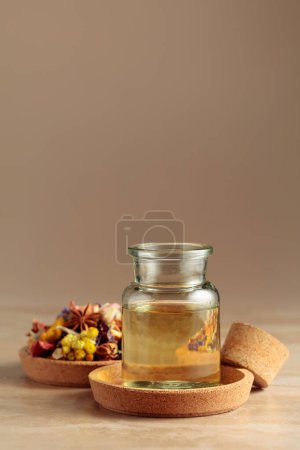 Essential oil or herbal tincture in a  small glass bottle. Mix of dried healthy medicinal herbs and healing plants on a beige background. Copy space.