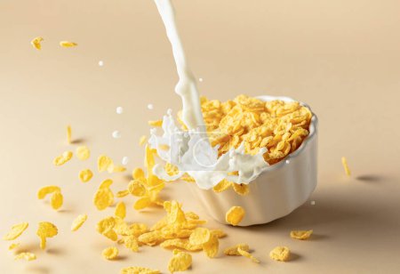 Foto de Copos de maíz de miel secos con salpicaduras de leche en un plato de cerámica. Copos con leche orgánica de granja. El concepto de alimentación saludable, comida vegetariana y vegana para el desayuno. - Imagen libre de derechos