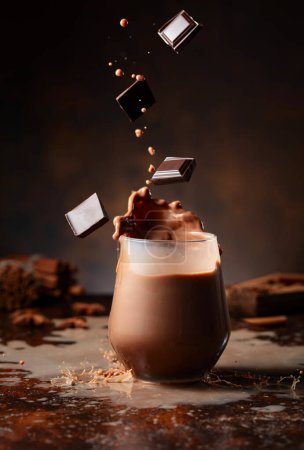 Photo for Pieces of dark chocolate fall into a glass of cocoa drink creating a beautiful splash. - Royalty Free Image