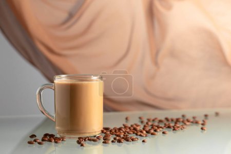 Foto de Café con crema sobre una mesa de cristal. En el fondo ondeando cortina beige. - Imagen libre de derechos