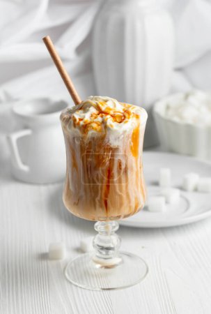 Photo for Iced caramel latte topped with whipped cream and caramel sauce, refreshing and sweet coffee drink on a white table. - Royalty Free Image