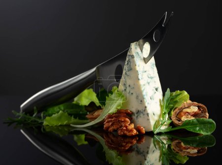 Foto de Queso azul con cuchillo, nueces y verduras frescas sobre fondo negro. Copiar espacio. - Imagen libre de derechos