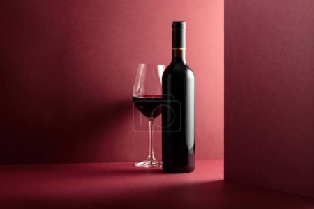 Foto de Botella y copa de vino tinto sobre fondo rojo. Copiar espacio
. - Imagen libre de derechos