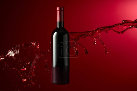 Foto de Botella de vino tinto y salpicadura sobre fondo rojo oscuro. Copiar espacio. - Imagen libre de derechos
