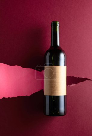 Foto de Botella de vino tinto con etiqueta vieja y vacía sobre fondo rojo oscuro. Vista superior. - Imagen libre de derechos