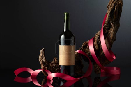 Photo for Bottle of red wine with old empty label. In the background old weathered snag with red satin ribbon. Concept of expensive wine. Frontal view with space for your text. - Royalty Free Image