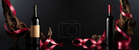 Photo for Bottles of red wine on a black reflective background. In the background old weathered snags with red satin ribbon. Concept of expensive wine. Frontal view with space for your text. - Royalty Free Image