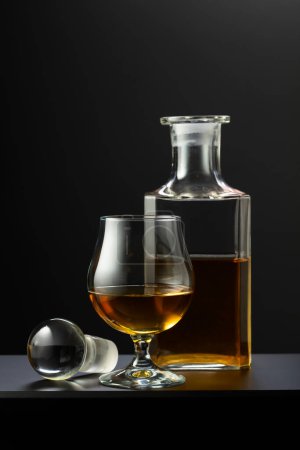 Photo for Old decanter and glass with whiskey, cognac or brandy on a black background. - Royalty Free Image