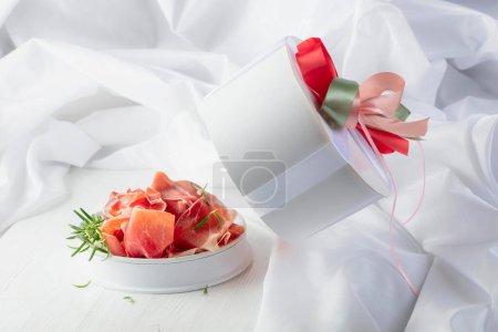 Téléchargez les photos : Prosciutto au romarin en coffret cadeau sur une table en bois blanc. Concept de cuisine italienne traditionnelle. - en image libre de droit