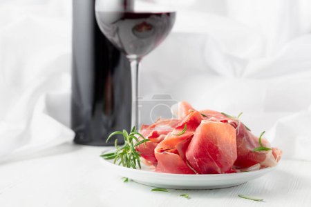 Photo for Prosciutto with rosemary and red wine on a white wooden table. Traditional Italian snack. - Royalty Free Image