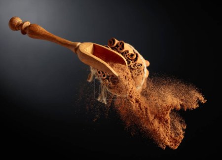 Photo for Cinnamon powder is poured out of the wooden spoon. The ground cinnamon and cinnamon sticks, tied with jute rope on a black background. - Royalty Free Image
