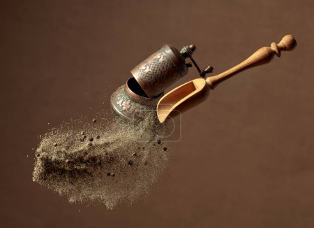 Photo for Pepper powder is poured out of the wooden spoon. Old copper pepper grinder and a wooden spoon with pepper ground. - Royalty Free Image