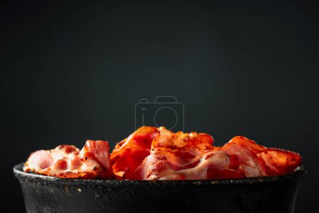 Photo for Fried bacon slices in old black pan on a black background. Copy space. - Royalty Free Image