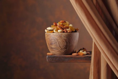 Foto de La mezcla de varias nueces y pasas en un tazón de madera sobre un fondo marrón. Copiar espacio. - Imagen libre de derechos