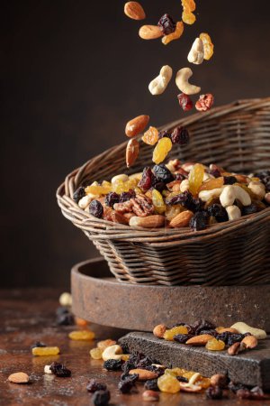 Photo for Mix of various nuts and raisins on a brown background. Dried fruit is poured in an old basket. Copy space. - Royalty Free Image