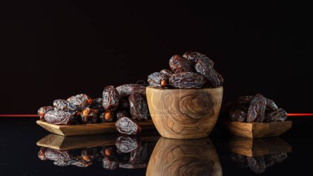 Photo for Dates in wooden dish on a black reflective background. - Royalty Free Image