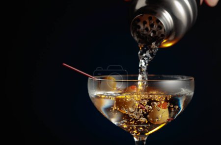 Foto de Martini con aceitunas verdes. El cóctel se vierte de una coctelera en un vaso. - Imagen libre de derechos