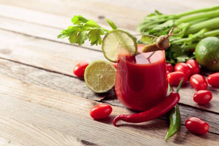 Foto de Cóctel Bloody Mary decorado con pepinillo, olivo, lima y apio. Bebida de tomate con ingredientes en una vieja mesa de madera. - Imagen libre de derechos