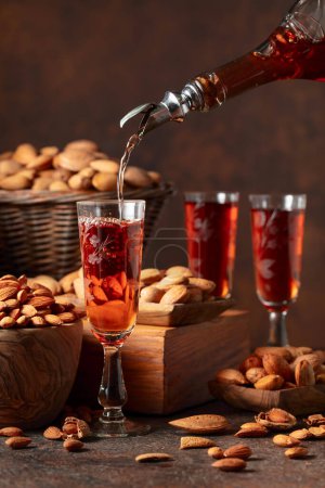 Téléchargez les photos : Liqueur italienne Amaretto aux amandes noix sur une table vintage. La liqueur est versée d'une bouteille dans un verre. - en image libre de droit