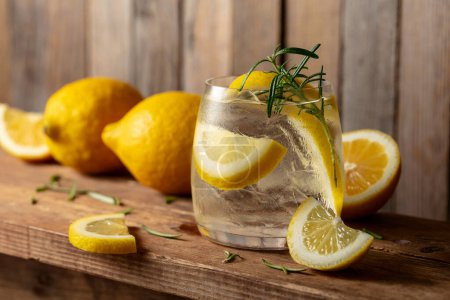 Téléchargez les photos : Cocktail gin tonique avec glace, romarin et tranches de citron sur une vieille table en bois. - en image libre de droit