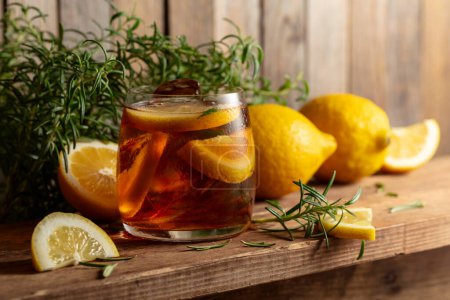Téléchargez les photos : Cocktail avec glace, romarin et tranches de citron sur une vieille table en bois. - en image libre de droit
