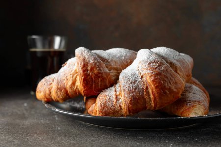 Photo for Fresh baked croissants and black coffee on a kitchen table. Croissants sprinkled with sugar powder. Selective focus. - Royalty Free Image
