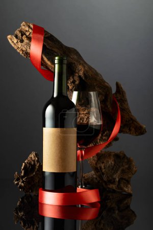 Photo for Bottle with old empty label and glass of red wine. In the background old weathered snag with red satin ribbon. Concept of expensive wine. - Royalty Free Image