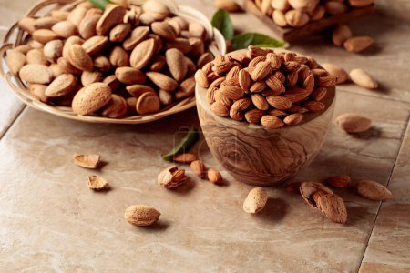 Photo for Almond nuts in wooden dishes on a brown ceramic table. - Royalty Free Image
