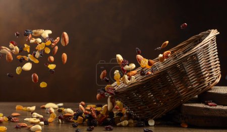 Photo for Dried fruits and nuts fall in basket. The mix of dried nuts and raisins on a brown background. Copy space. - Royalty Free Image