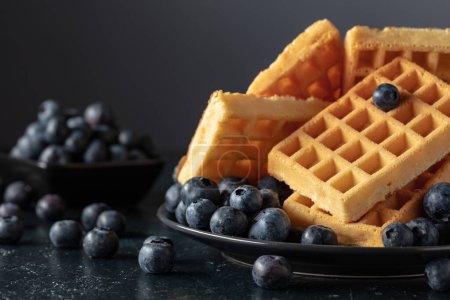 Photo for Belgian waffles with fresh blueberries on a black plate. Waffles and fresh berries on a dark blue table. - Royalty Free Image