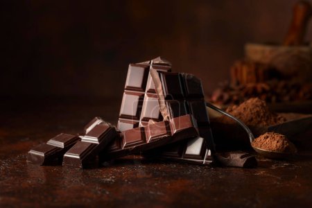 Téléchargez les photos : Barre de chocolat noir cassée et poudre de cacao sur une table brune. Espace de copie. - en image libre de droit