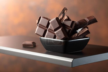 Photo for Broken dark chocolate bar in small black dish. Copy space. - Royalty Free Image