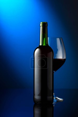 Téléchargez les photos : Verre et bouteille de vin rouge sur fond bleu. Vue frontale avec espace pour votre texte. - en image libre de droit
