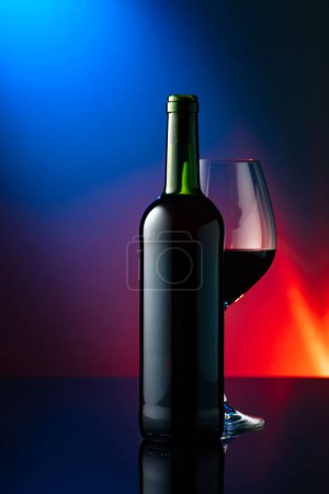 Foto de Copa y botella de vino tinto sobre fondo negro reflectante. Vista frontal con espacio para su texto. - Imagen libre de derechos