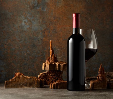 Foto de Copa y botella de vino tinto con trozos de madera vieja sobre un fondo oxidado. Coloque su etiqueta en el frasco. - Imagen libre de derechos